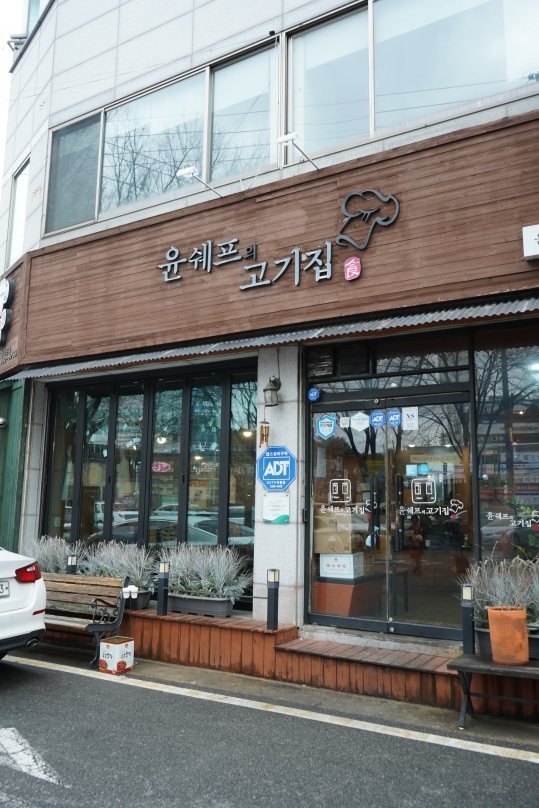 가게 바깥 — 나무 간판 «윤쉐프의 고기집»과 유리 출입문