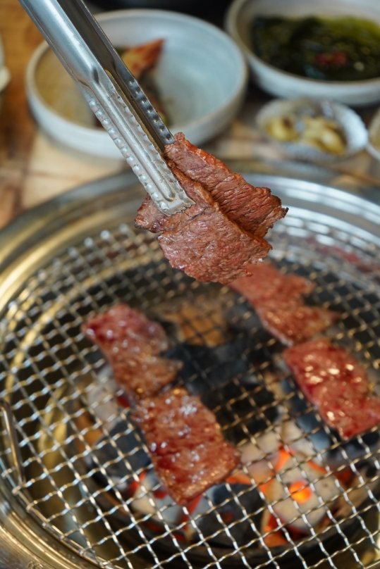 집게로 든 고기 한 점, 뒤로 밑반찬 그릇